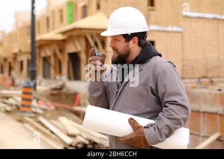 Builder che parla da walkie talkie e tenendo disegno piano nel cantiere. Foto Stock