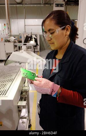 Matamoros, Messico, aprile 2006: Lavoratrice femminile detiene circuito stampato sulla linea di produzione in cui le autoradio sono in fase di produzione a Delphi Delco Electronics de Mexico, uno stabilimento di maquiladora attraverso il confine degli Stati Uniti che produce parti per le automobili General Motors. Delphi ha circa 11.000 lavoratori messicani in sette fabbriche vicino a Matamoros. ©Bob Daemmrich Foto Stock