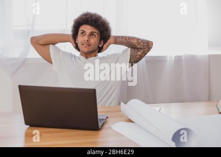 Uomo riccio appoggiato sulla sedia mentre si siede al suo posto di lavoro in ufficio. Tempo di relax, dopo il lavoro fatto. Foto Stock
