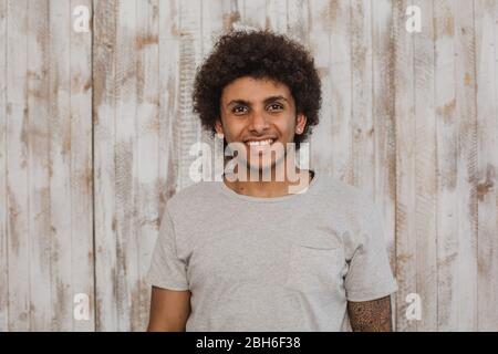 Mulatto con un sorriso perfetto. Ritratto allegro dai capelli ricci uomo guardando la telecamera, mentre in piedi contro il vecchio sfondo di legno Foto Stock