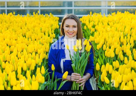 Donna giardiniere vestito in un uniforme di lavoro tenendosi in mano mazzo di tulipani e sorridendo guardando la macchina fotografica mentre in piedi in un grande giardino ce Foto Stock