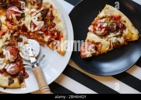 Il primo piano della pizza viene tagliato con un coltello rotondo. Riprese a stock. Deliziosa pizza calda tagliata con coltello rotondo professionale per fette lisce Foto Stock