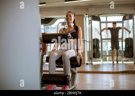 Donna giovane graziosa che ha esercitazioni sull'estensione della gamba e sulla macchina del riccio della gamba nella palestra Foto Stock