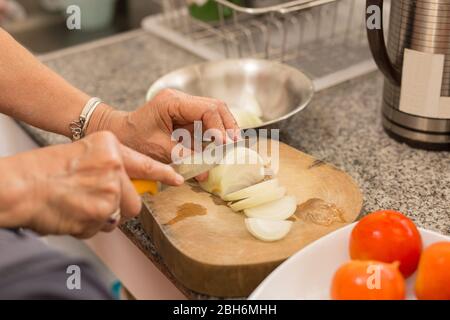 Donna anziana mani tritare la cipolla su un asse di legno in cucina. Foto Stock