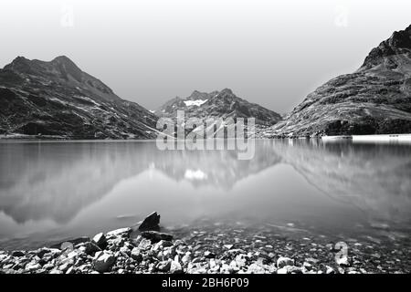 Paesaggio alpino panoramico con lago e montagne. Riflessi in un tranquillo lago di montagna. Fotografia in bianco e nero, monocromatica. Foto Stock