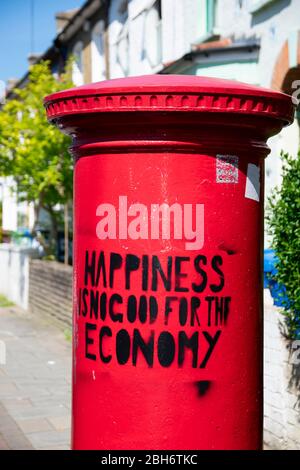 Londra / UK - 21 aprile 2020: 'La felicità non è un bene per l'economia'. Opere d'arte locali su una casella postale in Honor Oak. Foto Stock