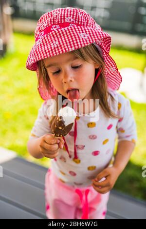 Bambino che mangia gelato su bastone . Bambina in cortile Foto Stock