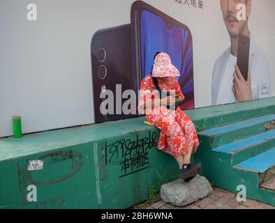 MISHAN, CINA - 28 LUGLIO 2019: La donna anziana asiatica utilizza uno smartphone per strada. Foto Stock