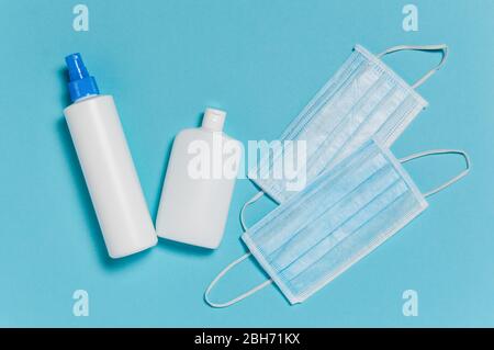 Protezione da coronavirus. Maschere chirurgiche mediche e flaconi di disinfettante e disinfettante per mani imbevuto di alcool su sfondo blu. Misure igieniche da prevenire Foto Stock