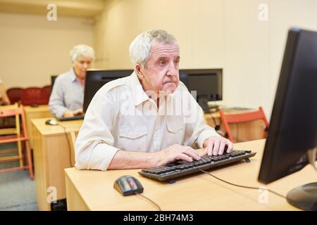 Uomo anziano seduto sul PC in un corso di computer VHS o in una casa di riposo Foto Stock