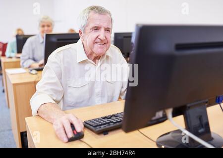 Un uomo senior sorridente sul PC impara l'uso di Internet in un corso sul computer Foto Stock