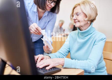 Il docente VHS aiuta i cittadini anziani a utilizzare il PC durante i corsi di informatica con l'uso di Internet Foto Stock