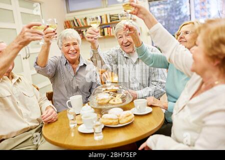Un gruppo di anziani allegri festeggiano con un bicchiere di vino bianco e una torta Foto Stock
