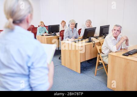 Docente e anziani su un PC in un corso di informatica presso il centro di istruzione per adulti Foto Stock