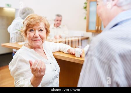 Due anziani parlano e si flirt con l'altro nella sala comune nella casa della gente anziana Foto Stock