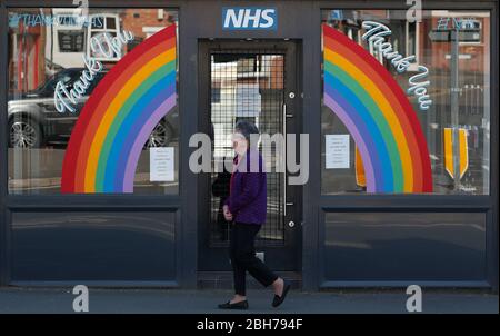 Anstey, Leicestershire, Regno Unito. 24 aprile 2020. Una donna cammina davanti a un negozio con un tributo al NHS durante il blocco pandemico del coronavirus. Credit Darren Staples/Alamy Live News. Foto Stock