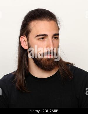 Modello giovane, alla moda maschile con capelli lunghi e barba che si posano in studio su sfondo isolato. Moda, business, concetto di modellazione. Foto Stock