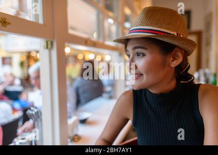 Primo piano di una giovane donna turistica asiatica felice che guarda fuori dalla finestra Foto Stock