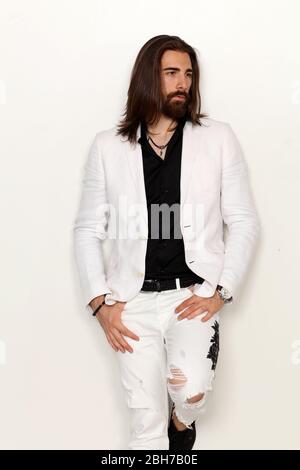 Modello giovane, alla moda maschile con capelli lunghi e barba che si posano in studio su sfondo isolato. Moda, business, concetto di modellazione. Foto Stock