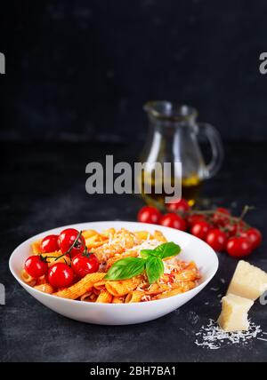 Pasta con salsa di pomodoro, basilico fresco, pomodori arrostiti e parmigiano su sfondo scuro con spazio per le copie. Penne è un tipo di pasta estrusa Foto Stock