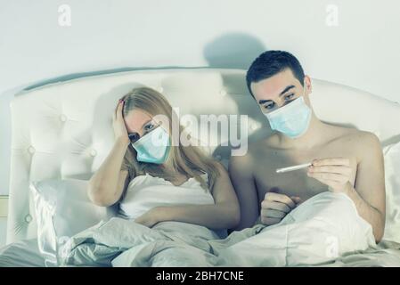 coppia a letto su auto-quarantena con maschere che soffrono di influenza o virus Foto Stock