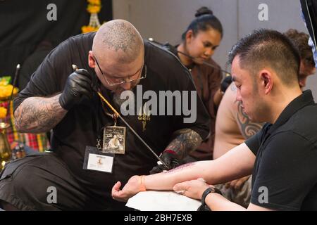 Un uomo che ottiene un tatuaggio del braccio da un tatuista usando la tecnica di tatuaggio del tubo del metallo alla 12th London Tattoo Convention 2016, banchina del tabacco, 50 Porter Foto Stock