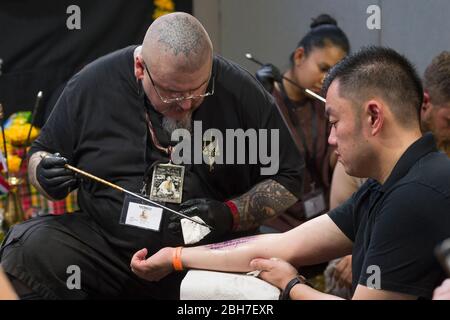 Un uomo che ottiene un tatuaggio del braccio da un tatuista usando la tecnica di tatuaggio del tubo del metallo alla 12th London Tattoo Convention 2016, banchina del tabacco, 50 Porter Foto Stock