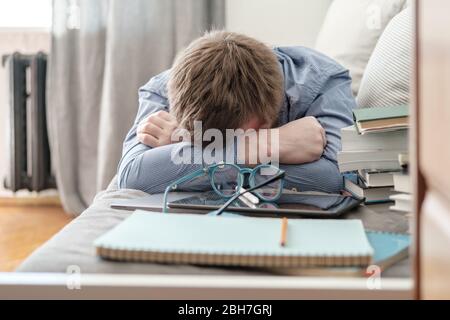 Lo studente era stanco e si addormentava a casa sul divano durante l'apprendimento a distanza. Concetto di formazione online durante la quarantena. Foto Stock