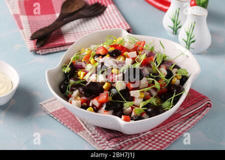 Insalata con fagioli neri, mais, bastoncini di granchio e microgrinie di piselli in una ciotola bianca su sfondo azzurro, formato orizzontale Foto Stock