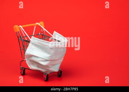 Carrello supermercato con maschera protettiva su sfondo rosso. Shopping durante il Coronavirus COVID-19 pandemic focolaio concetto Foto Stock