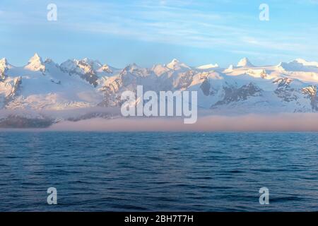 Montagne innevate, montagne innevate e nebbia marina, costa occidentale, Georgia del Sud e Isole Sandwich, Antartide Foto Stock