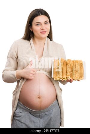 Donna incinta che mostra piatto di pancake e facendo un gesto okay come orgoglioso concetto di cuoco isolato su sfondo bianco Foto Stock