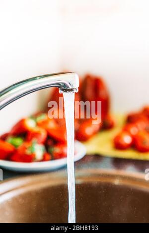 Lavare la frutta nel lavandino della cucina con acqua. Aprire il rubinetto con pomodori, fragole, peperoni. Foto Stock