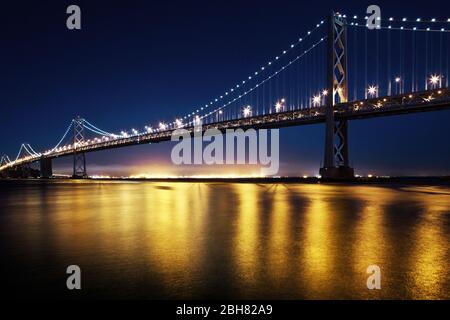 Una lunga esposizione del Bay Bridge a San Francisco di notte con luci che riflettono sull'acqua Foto Stock