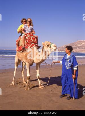 Camel driver con coppia turistica sulla spiaggia di Agadir, Agadir, Souss-massa-Draâ Regione, Marocco Foto Stock