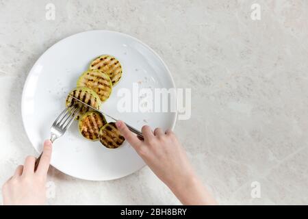 Zucchine fritte con sale grosso, appoggiate su un piatto bianco, nelle mani delle posate. Messa a fuoco selettiva. Foto Stock