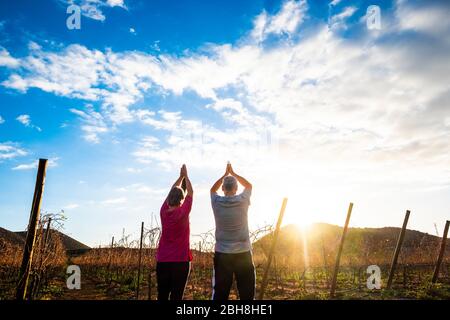 Yoga e meditazione posizione con due anziani uomo e donna insieme guardando e dando grazie al sole di mattina presto o tramonto d'oro - attività all'aperto sano per le persone lifestyle piacevole Foto Stock