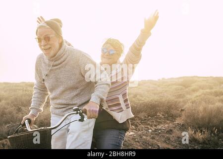 Felicità e libertà concetto senza limiti età con la coppia di vecchi anni ridendo sorridendo e avendo molto divertimento insieme su una bicicletta in attività di svago all'aperto - giovani e giocosi pensionati Foto Stock