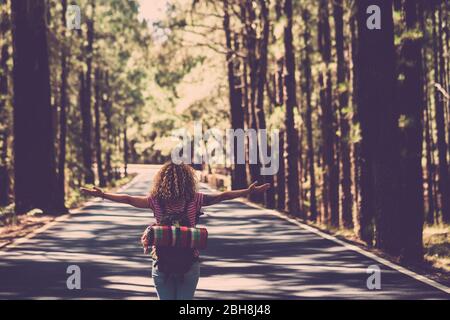 Eternità e successo soddisfazione vita concetto con la ragazza solitaria riccio hai rin il mezzo della strada lunga nella foresta con braccia aperte e zaino - wanderlust e viaggi stile persone Foto Stock