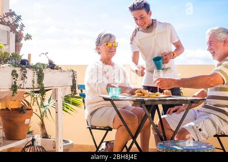 nonni adulti adulti e nipoti adolescenti. godetevi l'aria aperta in terrazza con cibo e bevande. vista sull'oceano e sulla città, vacanza giorno di sole bello clima concetto e sfondo. persone felici famiglia insieme Foto Stock