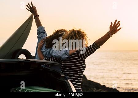 Felice coppia di ragazza ricci divertirsi insieme e guardare il tramonto di fronte all'oceano in vacanza tropicale bella all'aperto - abbraccio e amicizia per le persone felici Foto Stock