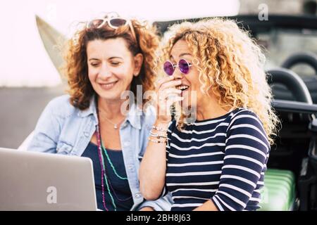 Un paio di donne giovani curly belle divertirsi ridendo utilizzando un notebook all'aperto - technoogy e concetto di persone - cose divertenti per le belle donne - ridere e sorridere stile di vita Foto Stock