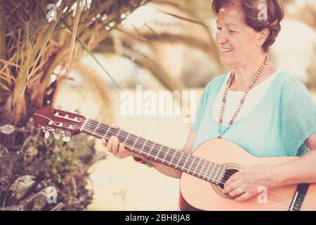 Senior caucasian bella allegra ragazza felice persone adulte cantare una chitarra all'aperto godendo l'attività di svago - terza età argento concetto società con sorridente maturo femmina - toni vintage Foto Stock