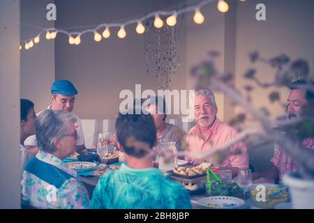 Cena serale per diverse età, amici caucasici giovani e vecchi tutti insieme divertirsi e gustare il cibo e le bevande sul tavolo - gruppo persone concetto di famiglia Foto Stock