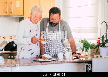 Coppia caucasica a casa preparare una torta insieme - padre e figlio adulti e senior lavorando in cucina - cucina uomini chef al lavoro con gioia e felicità Foto Stock