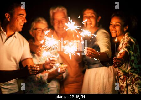 gruppo di persone divertirsi a festeggiare insieme la vigilia di capodanno o il compleanno con luci scintillanti e fuochi d'artificio in amicizia all'aperto a sera - famiglia e amici diverse età celebrare amichevole e sorridente Foto Stock