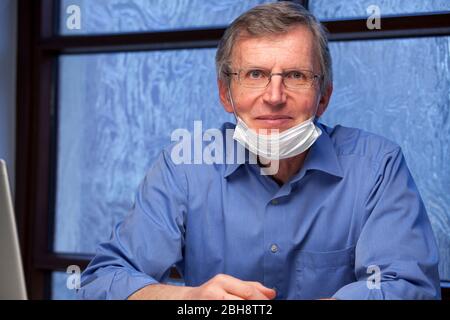 Ritratto di un medico sorridente amichevole alla sua scrivania con una maschera chirurgica - fuoco sul viso Foto Stock