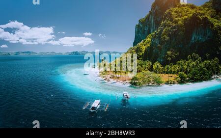EPIC foto panoramica drone aereo di barche turistiche in arrivo tropicale isola di Pinagbuyutan con idilliaca spiaggia di ipil circondata da acque turchesi blu oceano. El Nido, Palawan, Filippine. Foto Stock