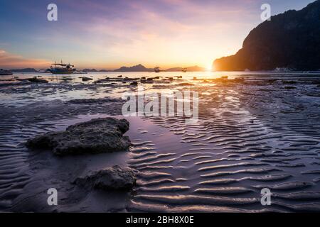 Spiaggia tropicale in tempo di riflusso bassa marea al tramonto. Le spiagge e i riflessi del sole all'ora d'oro. le isole della catena montuosa all'orizzonte. Coron Corong Beach, El Nido, Phillipines. Foto Stock