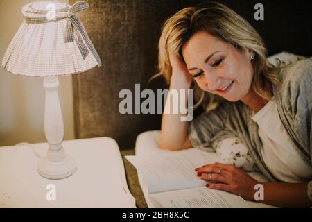 Frau liegt mit Buch im Bett Foto Stock
